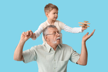 Grandfather and his happy cute little grandson playing with wooden airplane on blue background
