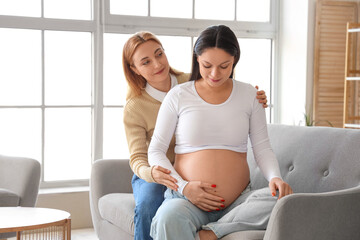 Young pregnant woman with doula sitting on sofa at home