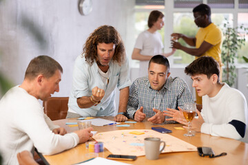 Obraz premium Expressive cheerful man with long wavy hair enthusiastically playing board game with male friends of different nationalities during bachelor party