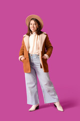 Young beautiful smiling woman in stylish jacket and hat on purple background