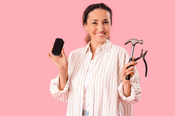 Happy female shoemaker with polishing brush, hammer and pliers on pink background