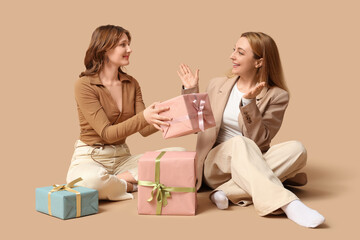 Beautiful mature woman and her daughter with gift boxes sitting on brown background. Mother's Day...