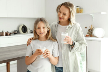 Happy mother and her daughter with cups of milk in kitchen at home