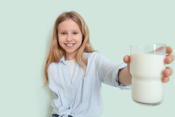 Happy little girl with cup of milk on turquoise background