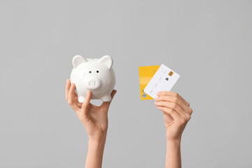 Female hands with credit cards and piggy bank on grey background, closeup