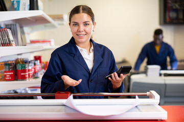 Cheerful young female specialist in uniform calculates the cost of notepads and sheets in the...