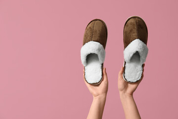 Female hands holding brown slippers on pink background