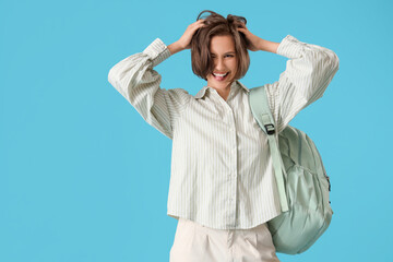 Happy female student with backpack showing tongue on blue background