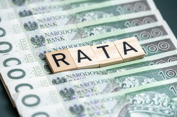 Wooden blocks spelling "RATA" on a background of Polish zloty banknotes, highlighting financial concepts related to installment or rate payments