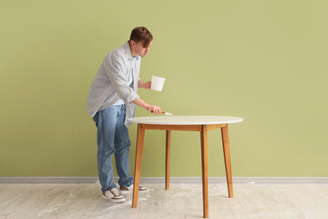 Young man with brush painting table near green wall