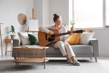 Young woman playing guitar on sofa in living room