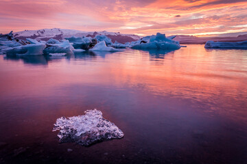 Breathtaking view of a vibrant sunset reflecting on a serene glacial lagoon with icebergs