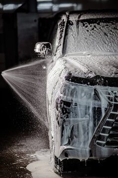 Man applying foam to black car in car wash. Vertical photo. 