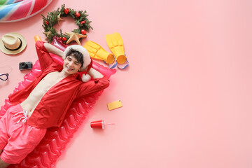 Young man in Santa hat with beach accessories lying on pink background, top view. Christmas in July