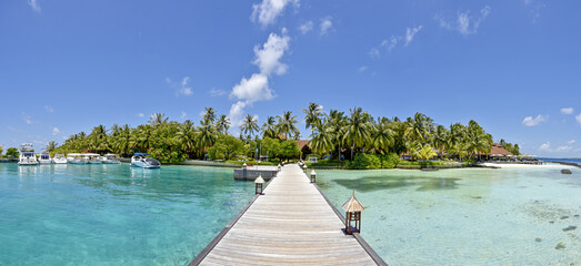 Panoramic view of a serene tropical island resort with a wooden jetty extending into turquoise waters