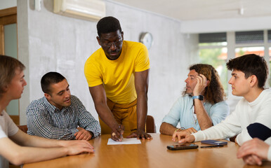 Obraz premium Middle-aged trainer explaining the topic to group of guys sitting around the table in auditorium
