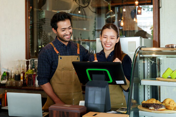 Beautiful woman and husband are smiling happily at the shop counter. in the morning of day. Asian and Indian small business owner couple preparing to open a family cafe, getting ready to work in cafe