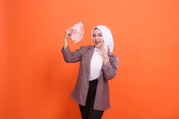 Excited beautiful Asian woman wearing hijab cheerful holding rupiah banknotes and palm in front of...