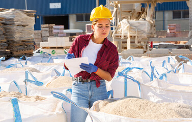 Young attractive female supervisor with documents checking quality of building mix at hardware...