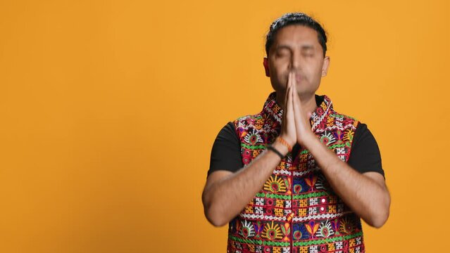 Indian man putting hands together in begging gesture, making wish, isolated over studio background. Faithful person asking for something, praying and hoping, believing in higher power, camera A
