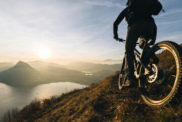 Silhouette of a cyclist enjoying a sunrise ride on a mountain trail with a scenic lake view