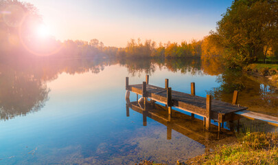 Serene sunrise over tranquil lake with wooden pier