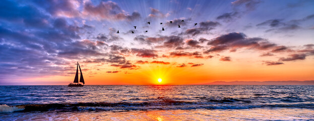 Serene panorama with a sailboat and flying birds against a vibrant sunset