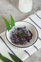 Black sticky rice porridge, a typical Indonesian dessert. Black sticky rice porridge with coconut milk, sugar and pandan leaves. Served in a white bowl.