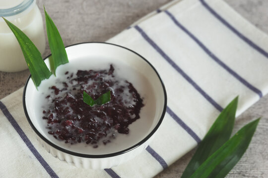 Black sticky rice porridge, a typical Indonesian dessert. Black sticky rice porridge with coconut milk, sugar and pandan leaves. Served in a white bowl.