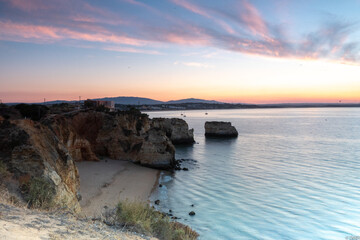Tranquil morning scene of a beach with cliffs under a pastel sunrise sky