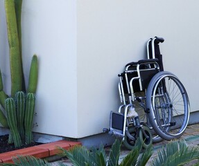 Carrozzella per disabili sta appoggiata sul muro bianco di una casa vicino ad un cactus