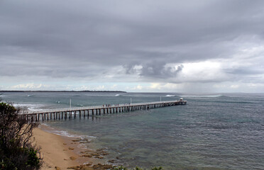 Pier jetty extending into the sea under a cloudy stormy sky at Point Lonsdale in Victoria, Australia