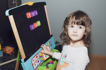 Toddler girl learning letters on the magnetic easel at home.