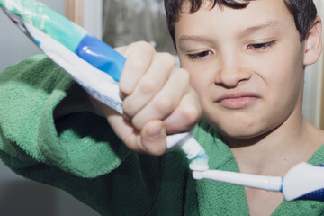 Boy in green bathrobe with an electric toothbrush squeezing toothpaste.