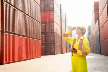 foreman control loading containers box from cargo freight ship working at dock site,young asian man in safety uniform holding walkie talkie standing and looking at shipping containers