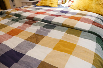 a bed with a colorful plaid comforter and pillows in shades of Purple, Orange, and Yellow,