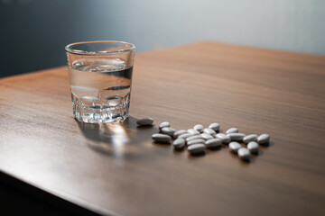 white pills and caplsules, glass of water on wooden table