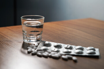 white pills and caplsules, glass of water on wooden table