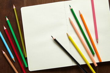 Eleven colored pencils and an empty sketchbook on a wooden table