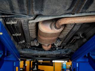 Bottom view of exhaust pipe under the car while lifted vehicle check-up maintenance service. A part...