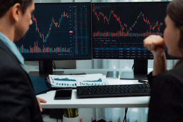 Two business traders discussing on dynamic stock market in currency rate investment trading on two pc screens with compare real time graph on risk or profit point of data at modern office. Postulate.