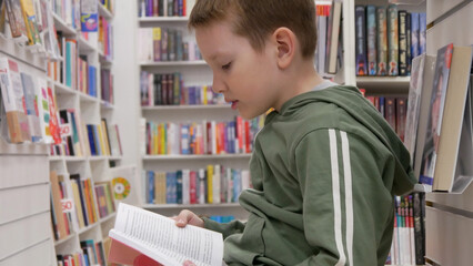 Close-up of a cute boy reading a book in a book shop or library
