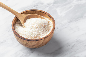 Psyllium husk in wooden bowl with spoon on white marble table