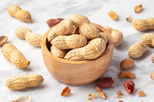 Peanuts in wood bowl with shell on white marble table