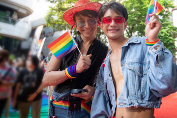 LGBTQ men have fun celebrating their pride with flags at the annual Pride Parade, waving rainbow flags in hands, celebrate LGBTQ Pride Month Parade, smiling and looking at camera