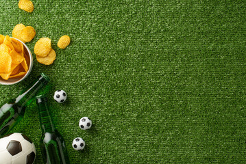 Top view of a football-themed snack arrangement with chips in a bowl, mini soccer balls, and beer bottles on a grass textured surface