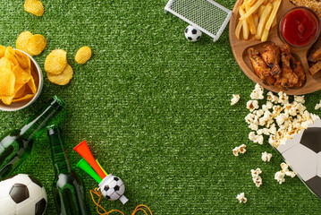 Top view of football fan essentials on green grass texture featuring snacks and soccer accessories