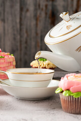 Serving tea in a cup that is surrounded by cupcakes.