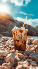 A chilled coffee beverage garnished with caramel, cream, and ice, placed on a rocky surface with...