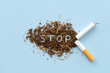 Broken cigarette scattered tobacco with text STOP on a light blue background. Quit smoking concept....